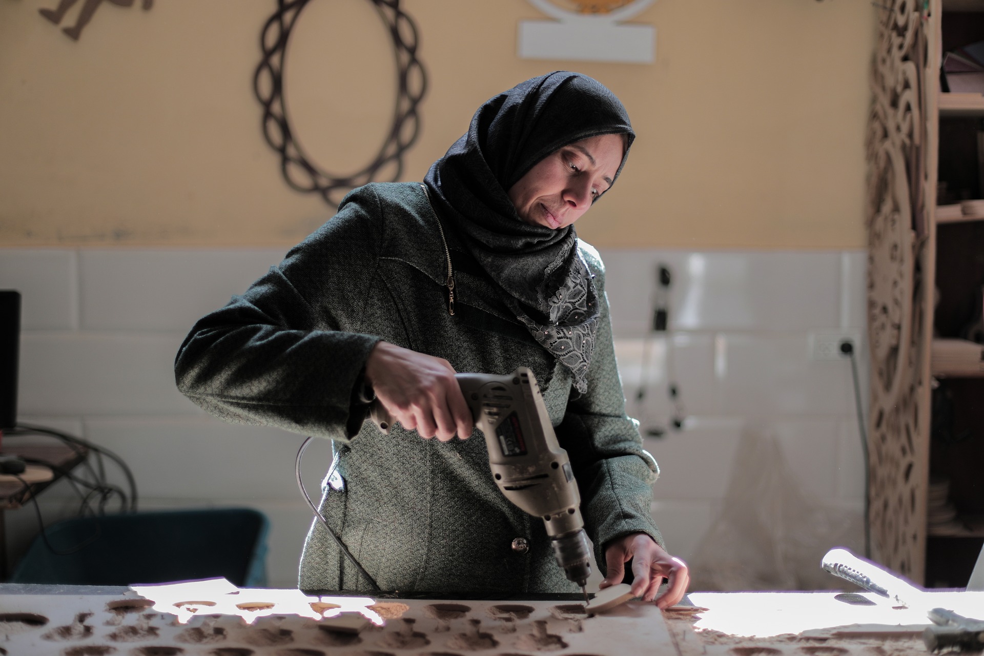 Bild zeigt Frau mit Kopftuch, die in einer Werkstatt mit einem Bohrer arbeitet